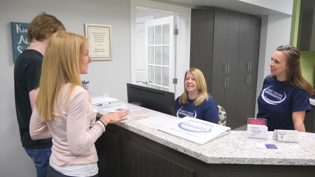 Team Demas front desk administrator talking to a patient and his mom